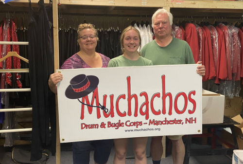 Mari Abbott with her parents, Karen and Charlie, holding a Muchachos Drum and Bugle Corps sign.